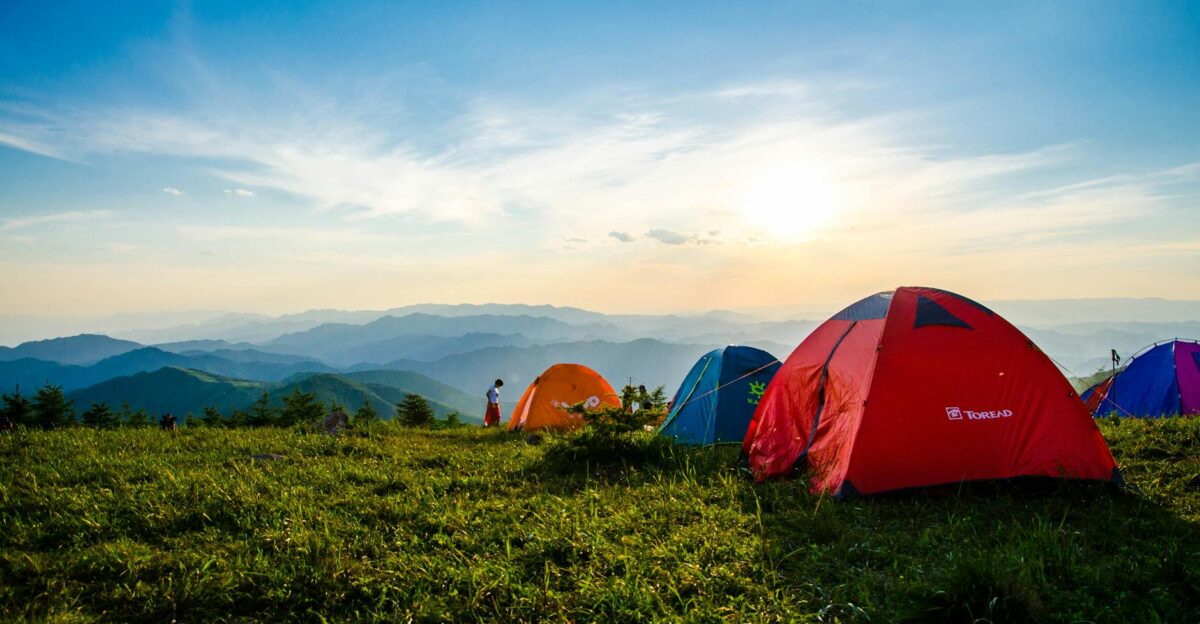 Vibrant tents on a grassy mountain ridge with a stunning sunrise view ideal for adventure