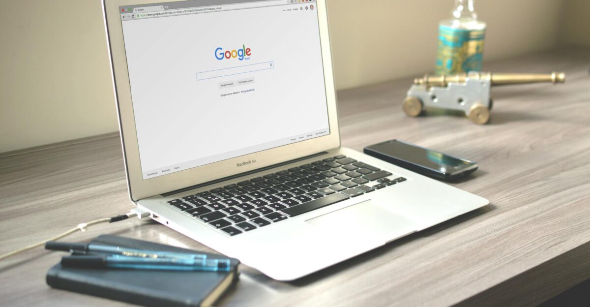 A neat workspace featuring a laptop displaying Google search a smartphone and a notebook on a wooden desk