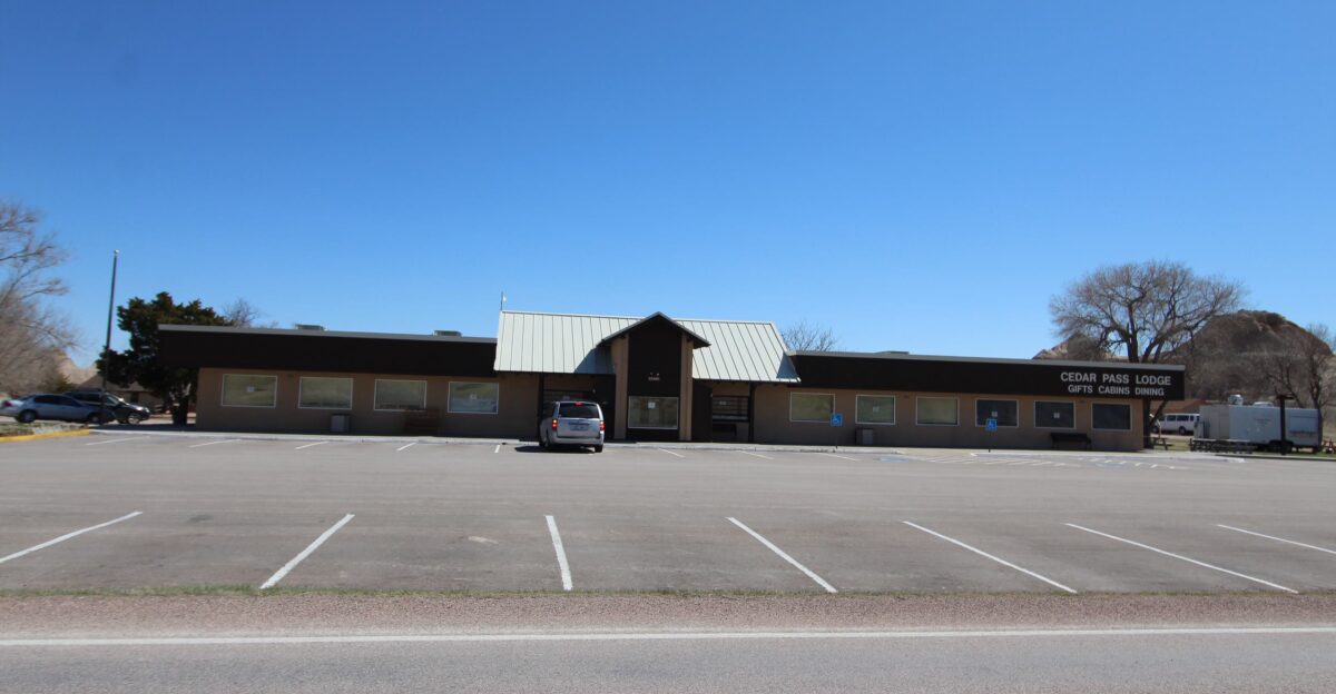 a long brown building with a sign reading Cedar Pass Lodge Gifts Cabins Dining The Cedar Pass Lodge is where you can eat meals check out a souvenir shop and book reservations for cabins or camping