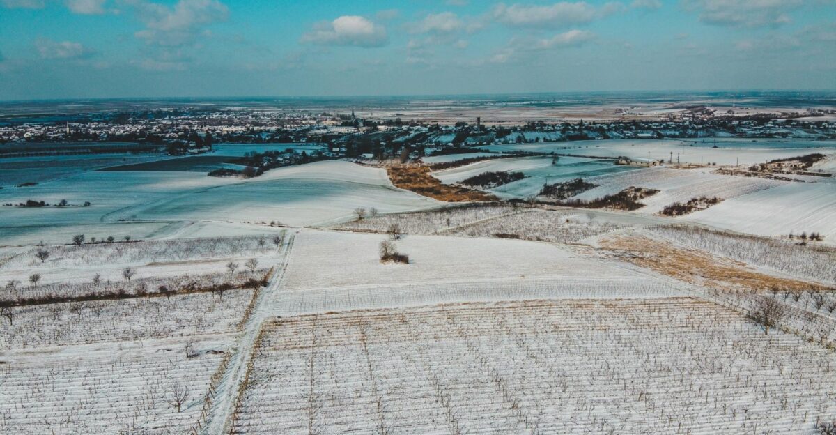 A stunning aerial view of snowy fields in S cueni Romania with a distant village under a blue sky