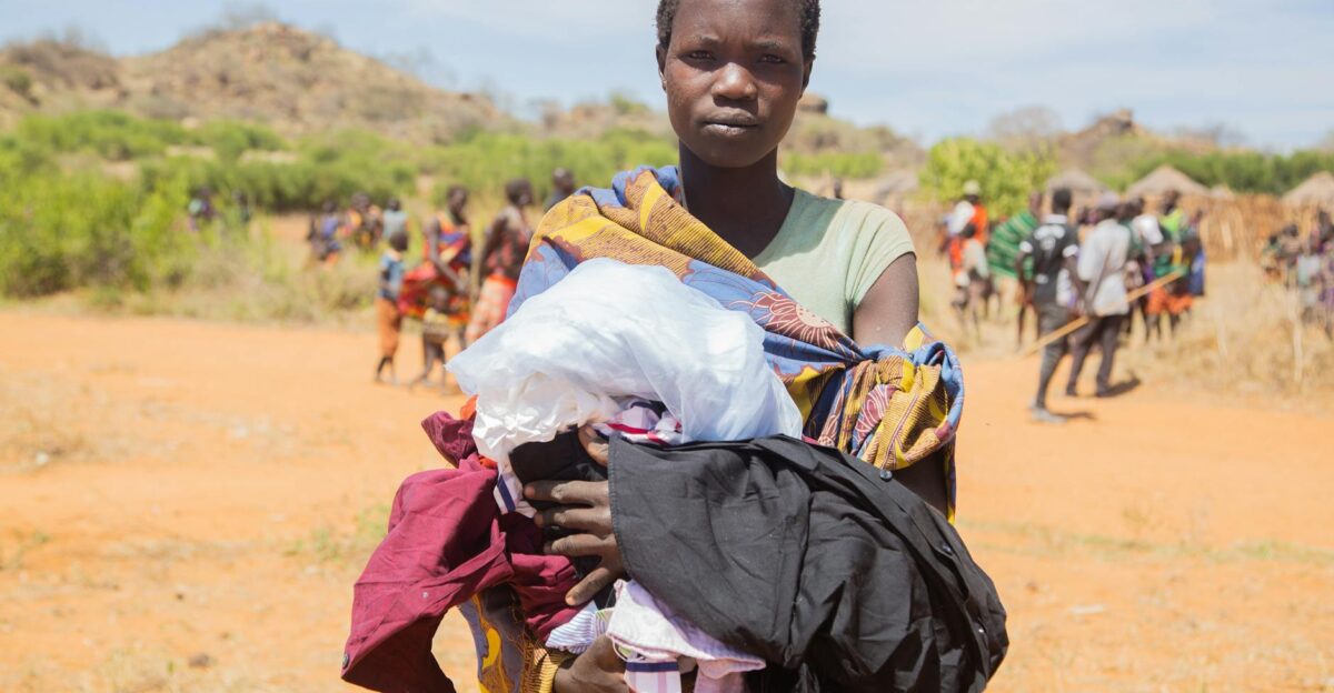 African woman holding clothes in a rural village setting under bright daylight