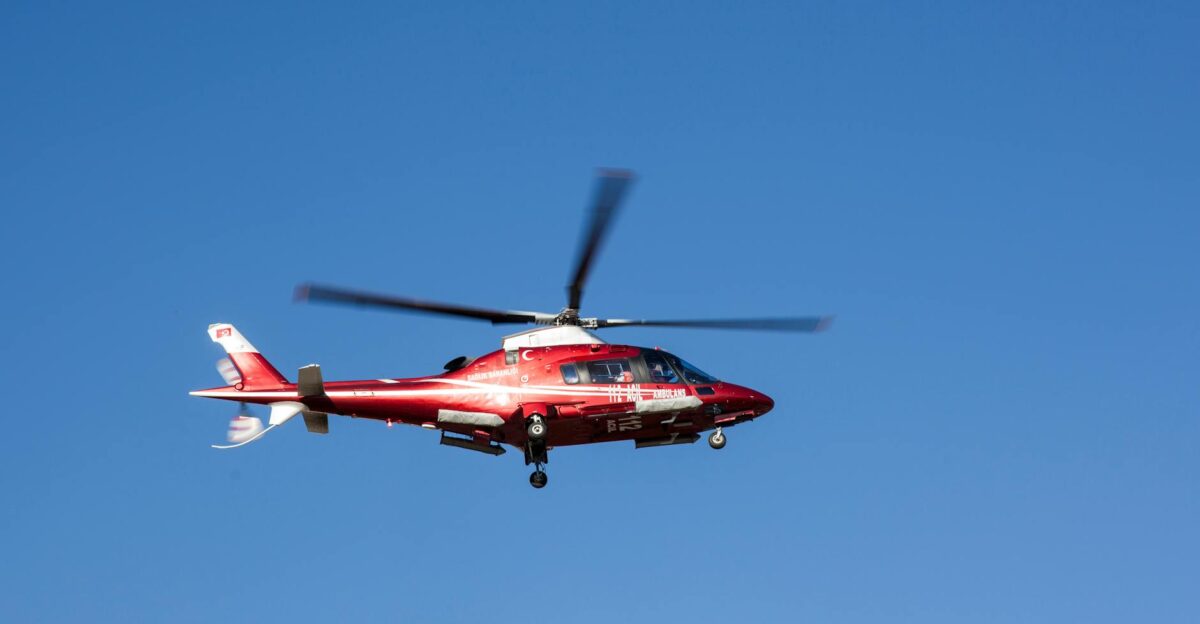 Red helicopter flying against clear blue sky symbolizing emergency medical rescue