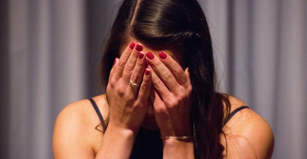 woman in black tank top covering her face with her hands