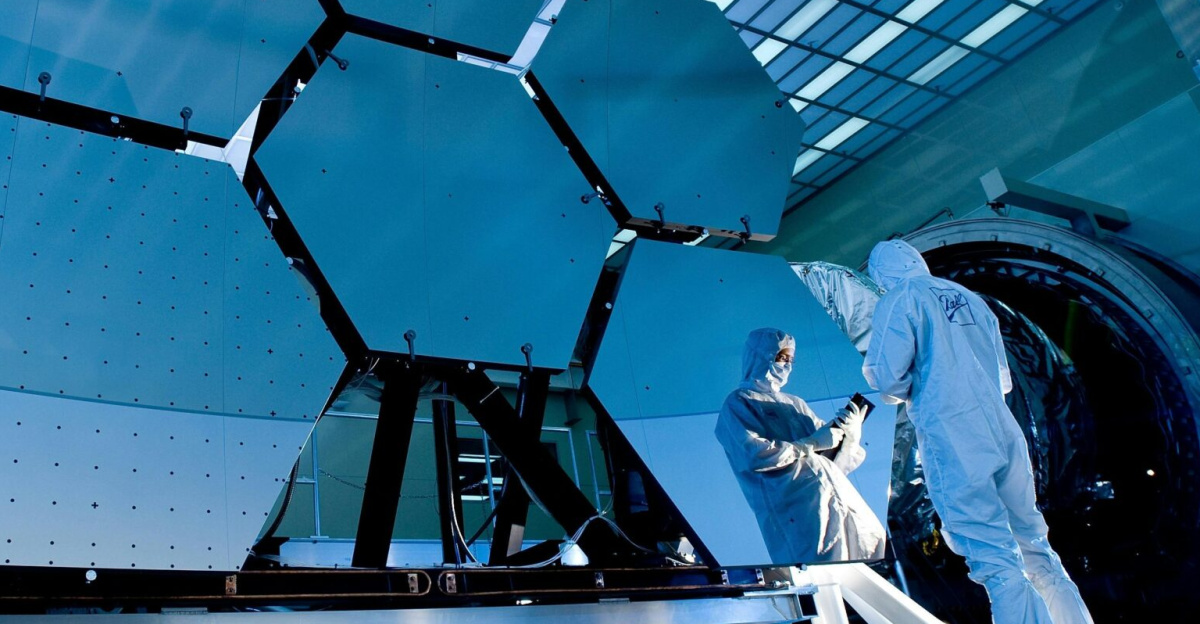 Engineers in protective suits work on telescopic mirrors in a high-tech lab.